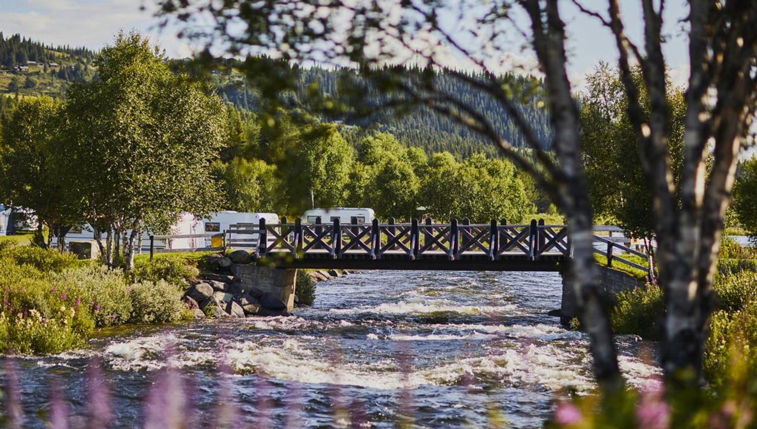 Elva som renner under brua ved campingplassen. Kan skimte campingvognene i bakgrunn