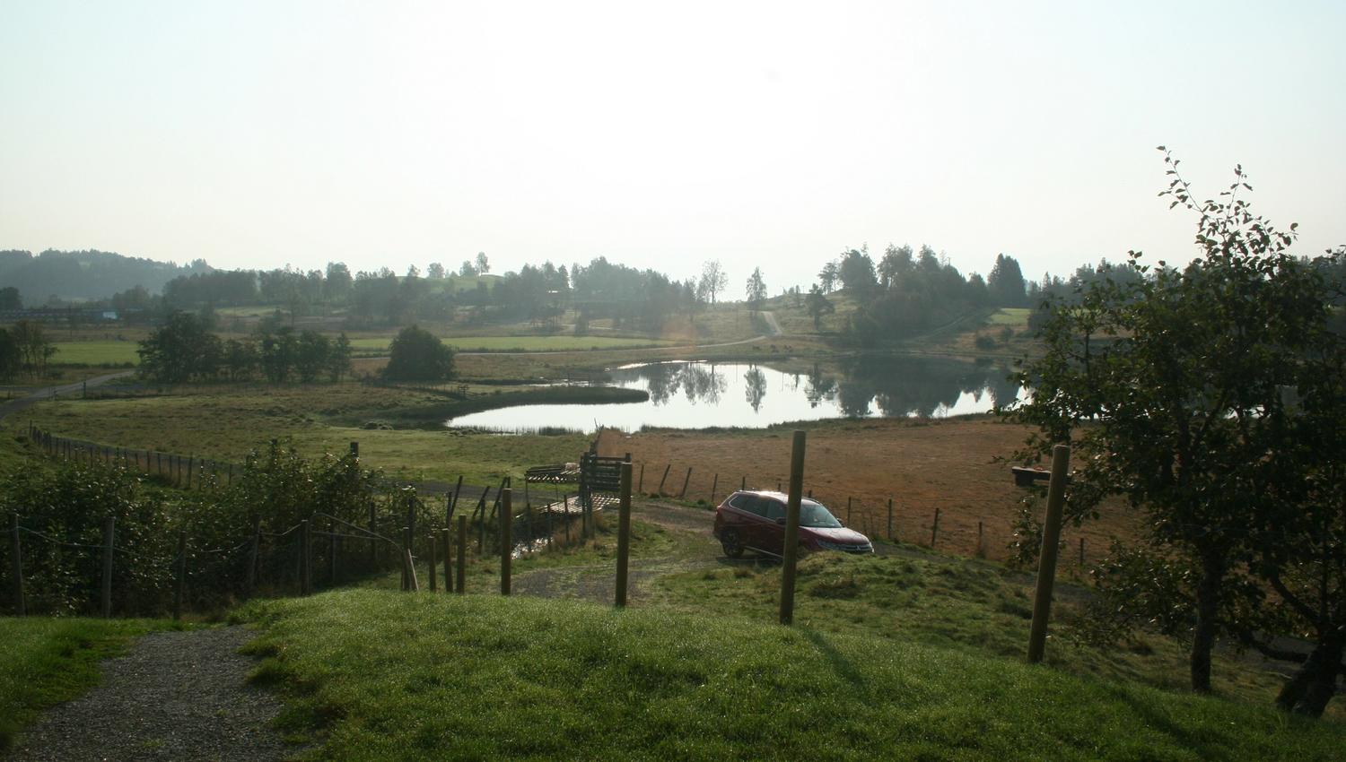 View from Sjusete Cabins over a picturesque lake with rolling hills and forest in the distance.