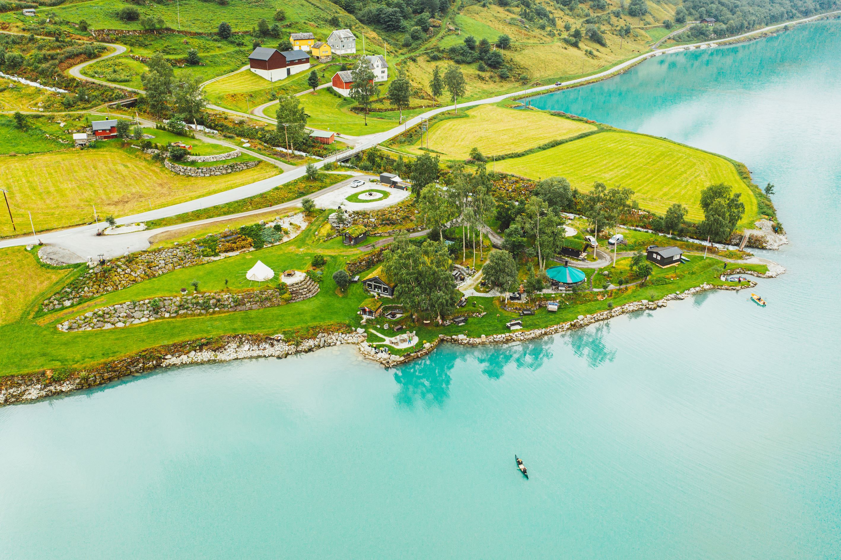 Aerial view of green farmland and small houses on a peninsula beside a turquoise lake, with roads and trees.