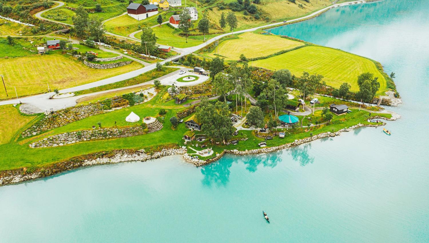 Aerial view of green farmland and small houses on a peninsula beside a turquoise lake, with roads and trees.