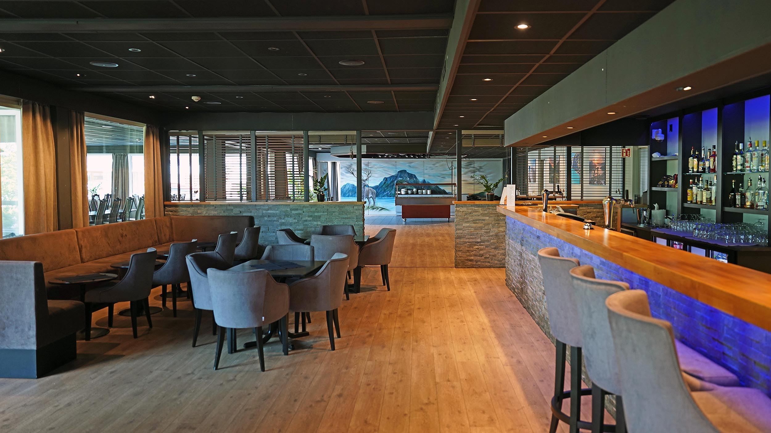 Moderne restaurantlounge på Bremanger Fjordhotell i Svelgen med bar til høgre, bord og stolar til venstre, tregolv og dempa belysning..