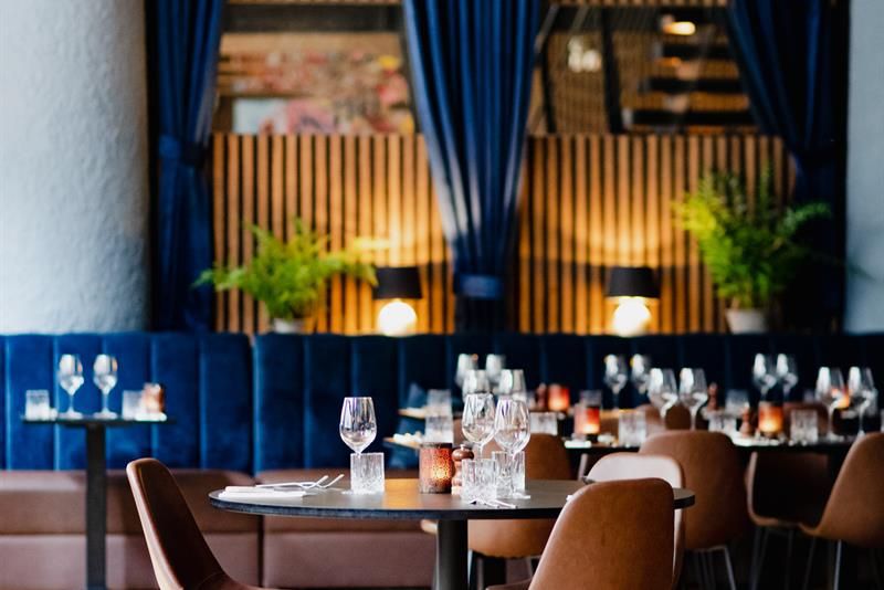 Round, black dining table and brown chairs, blue seating section along the wall