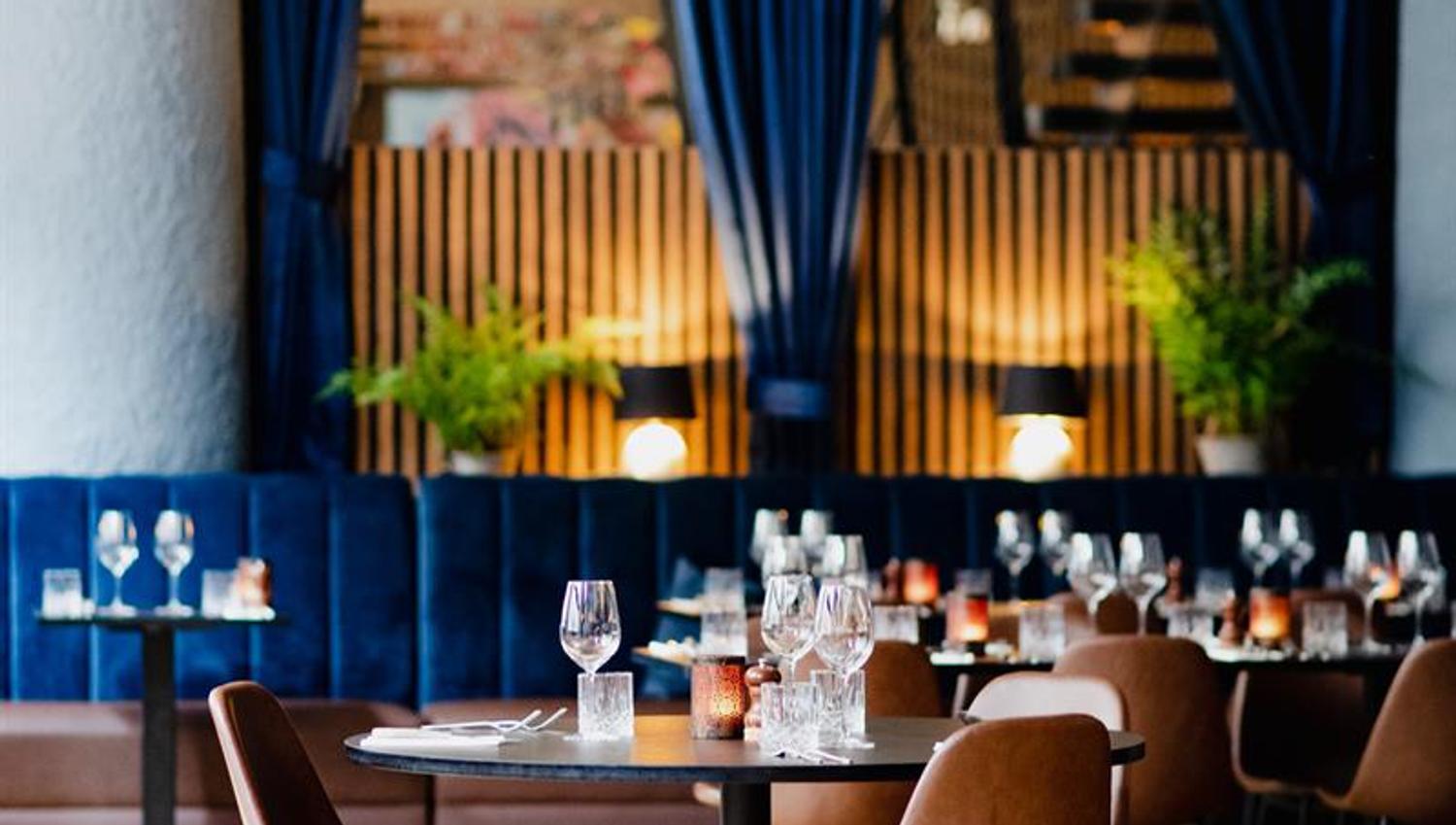 Round, black dining table and brown chairs, blue seating section along the wall