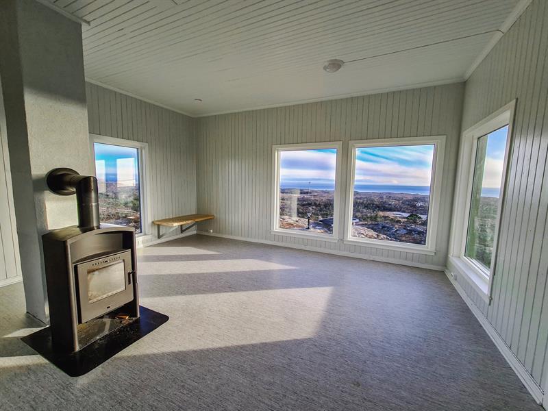 Inside the day trip cabin: a living room with a wood-burning stove and windows on all sides, offering views out toward the sea.