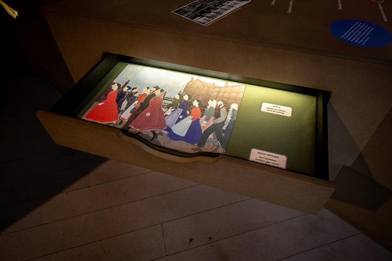 Interactive museum installation with an illuminated drawer displaying illustrations and text-based activities.