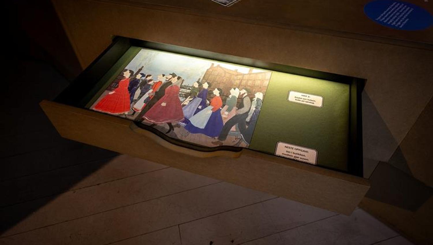 Interactive museum installation with an illuminated drawer displaying illustrations and text-based activities.