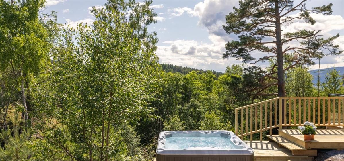 A hot tub on a terrace surrounded by trees with a view of the landscape.