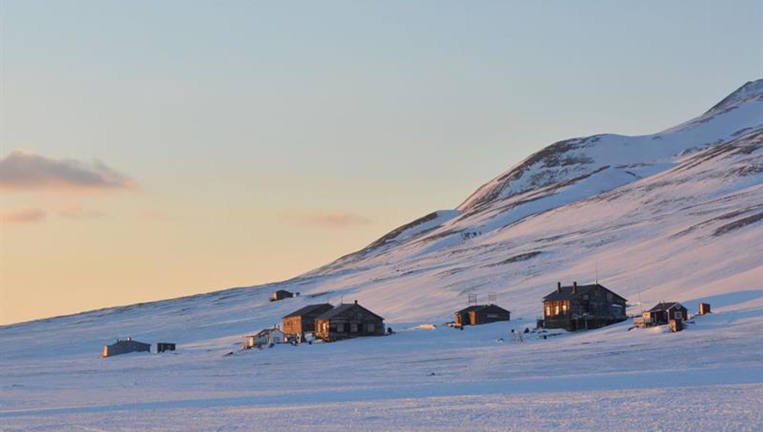 Several cabins at the foot of a mountain, with sunlight shining on the cabin walls.