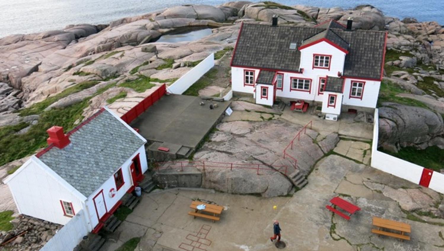 Oversiktsbilde over huset på Ryvingen fyr. Huset er hvitt med røde detaljer (røde lister) og svart tak.