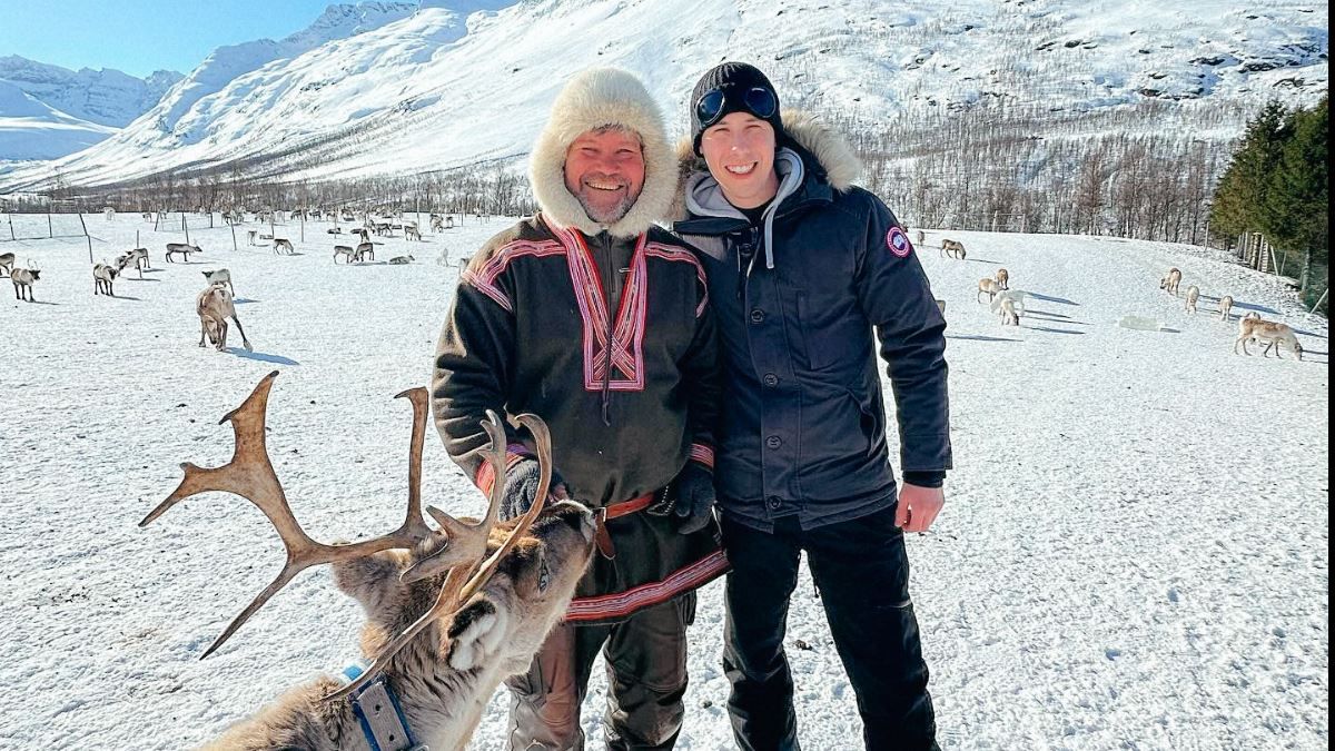A Sami guide standing with a guest while a reindeer is looking at them