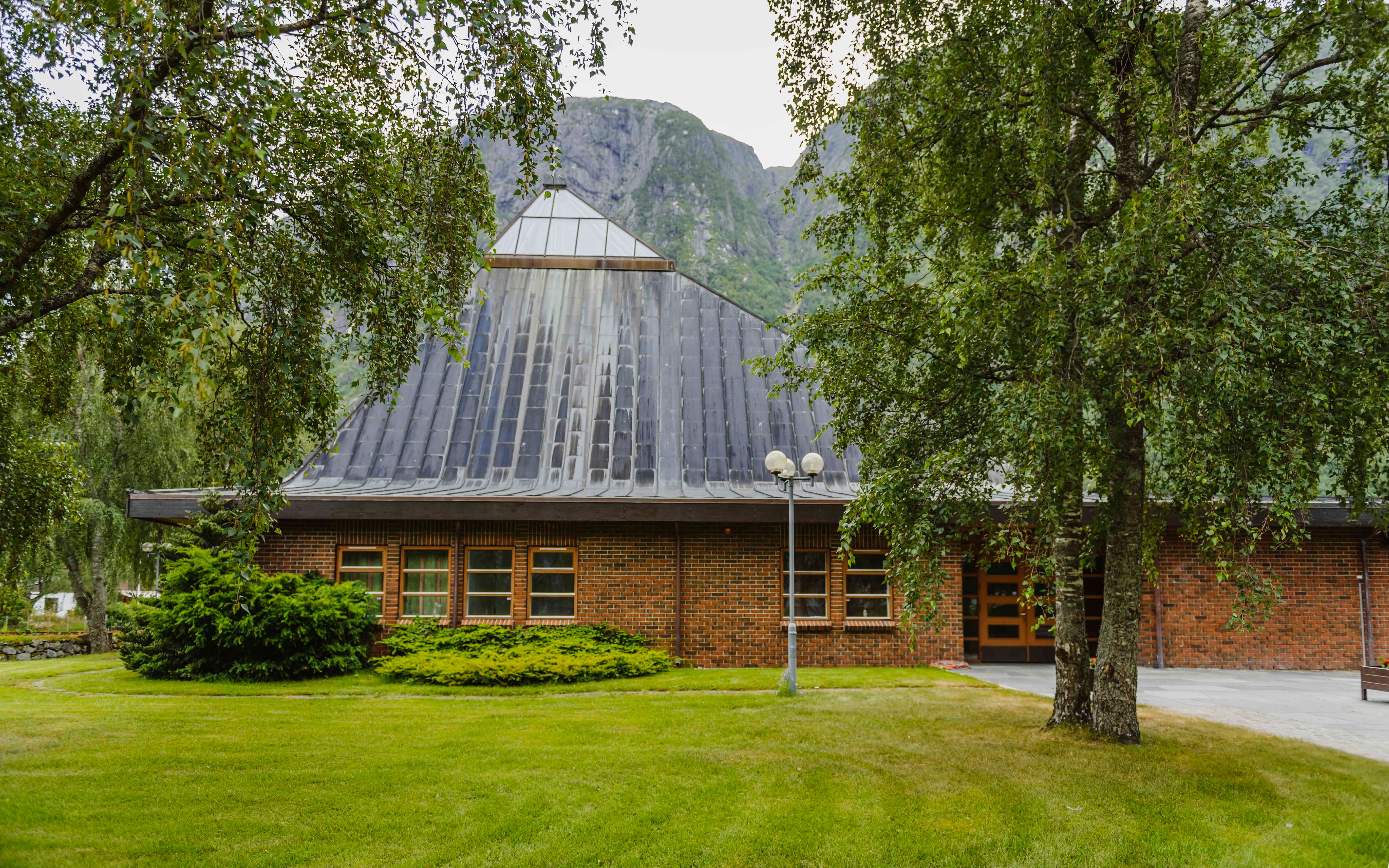 Eidfjord new church seen from the outside, with nice greenery and a tall mountain in the background.