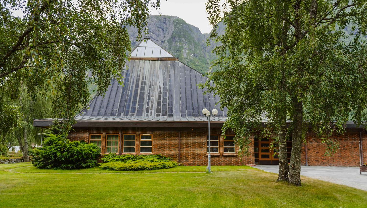 Eidfjord new church seen from the outside, with nice greenery and a tall mountain in the background.