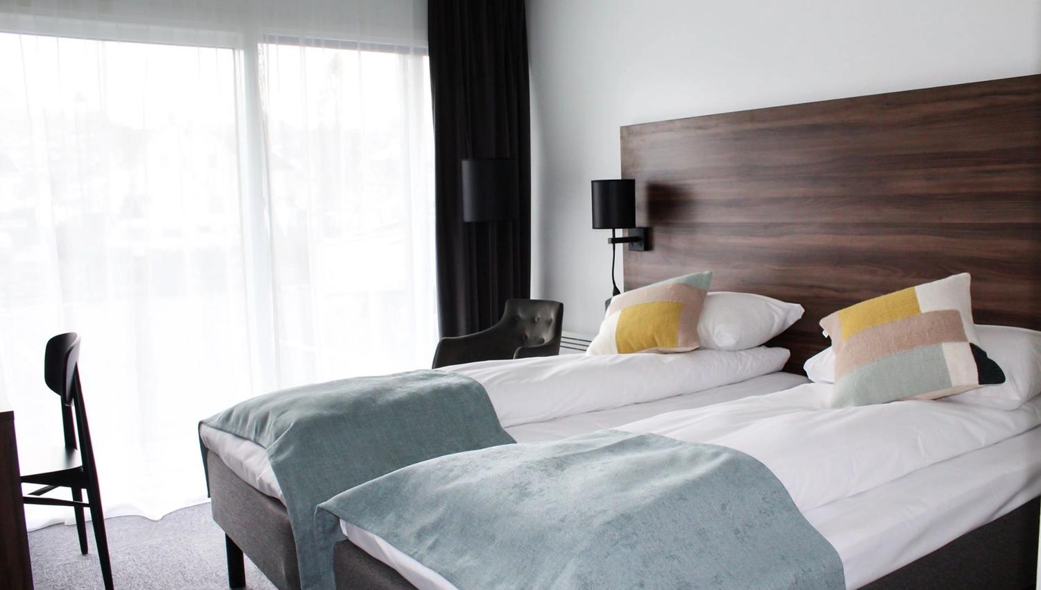 Bright hotel room with two single beds and a fjord view from the balcony.