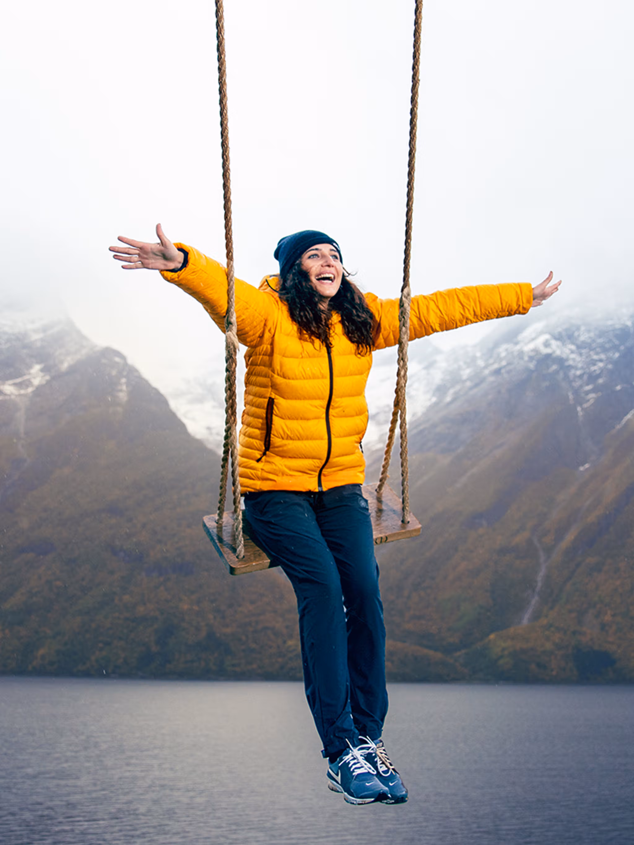 Eine Person auf einer Schaukel mit Blick auf schneebedeckte Berge und den Hjørundfjord in Fjord Norwegen