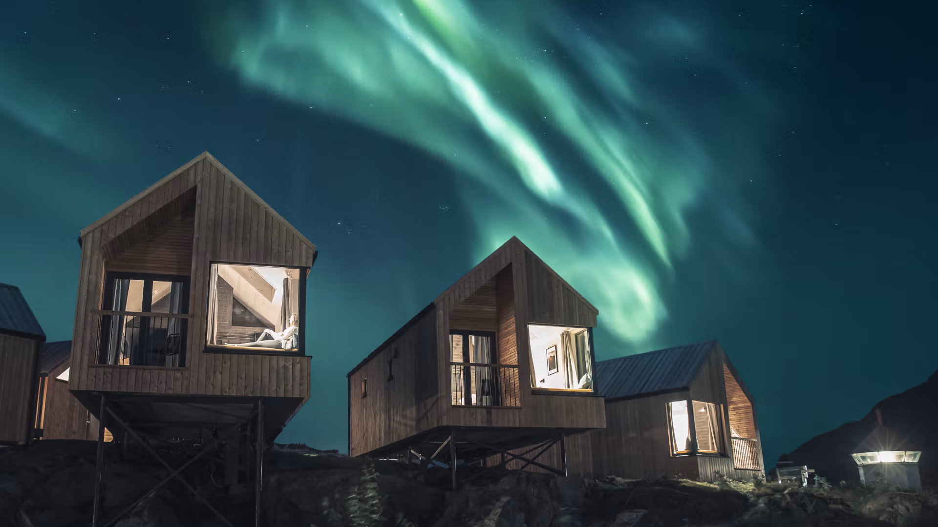 Person chilling in one of the cabins at Hattvika Lodge, with Northern Lights dancing on the sky