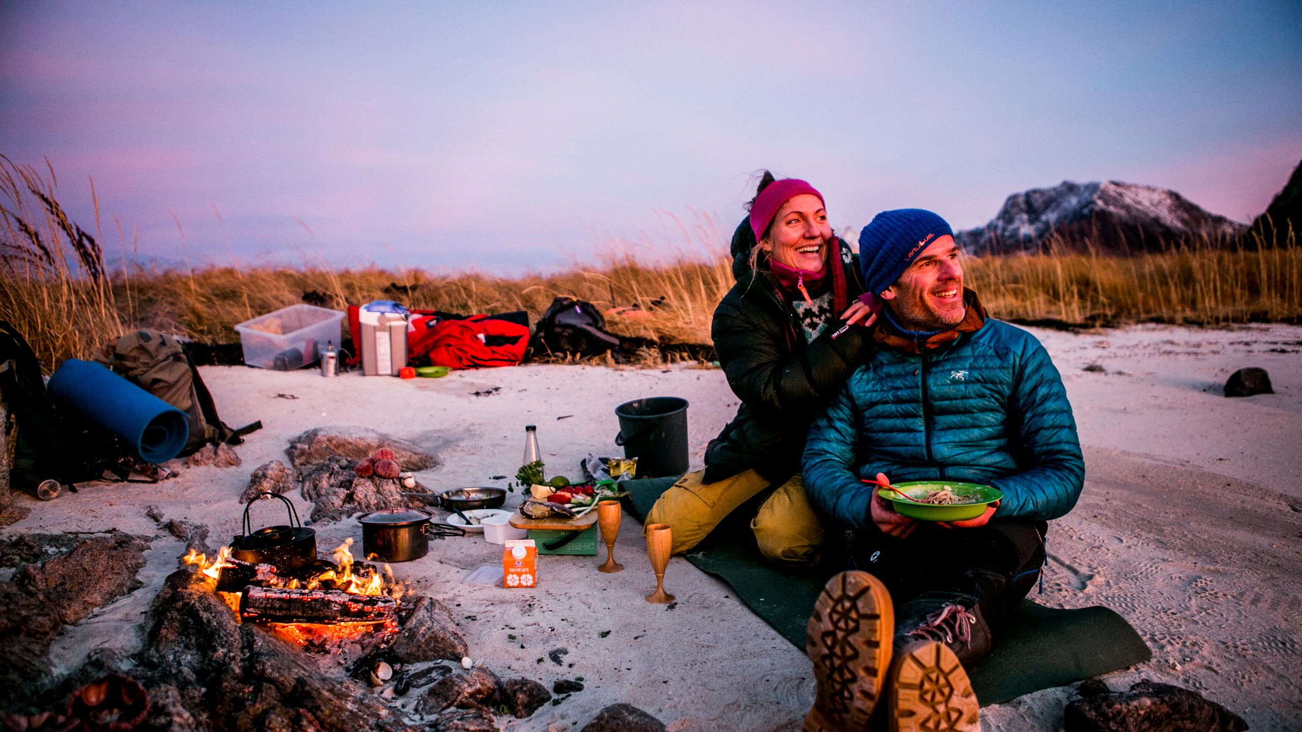 Two campers having a cosy campfire dinner on a beach in the evening light