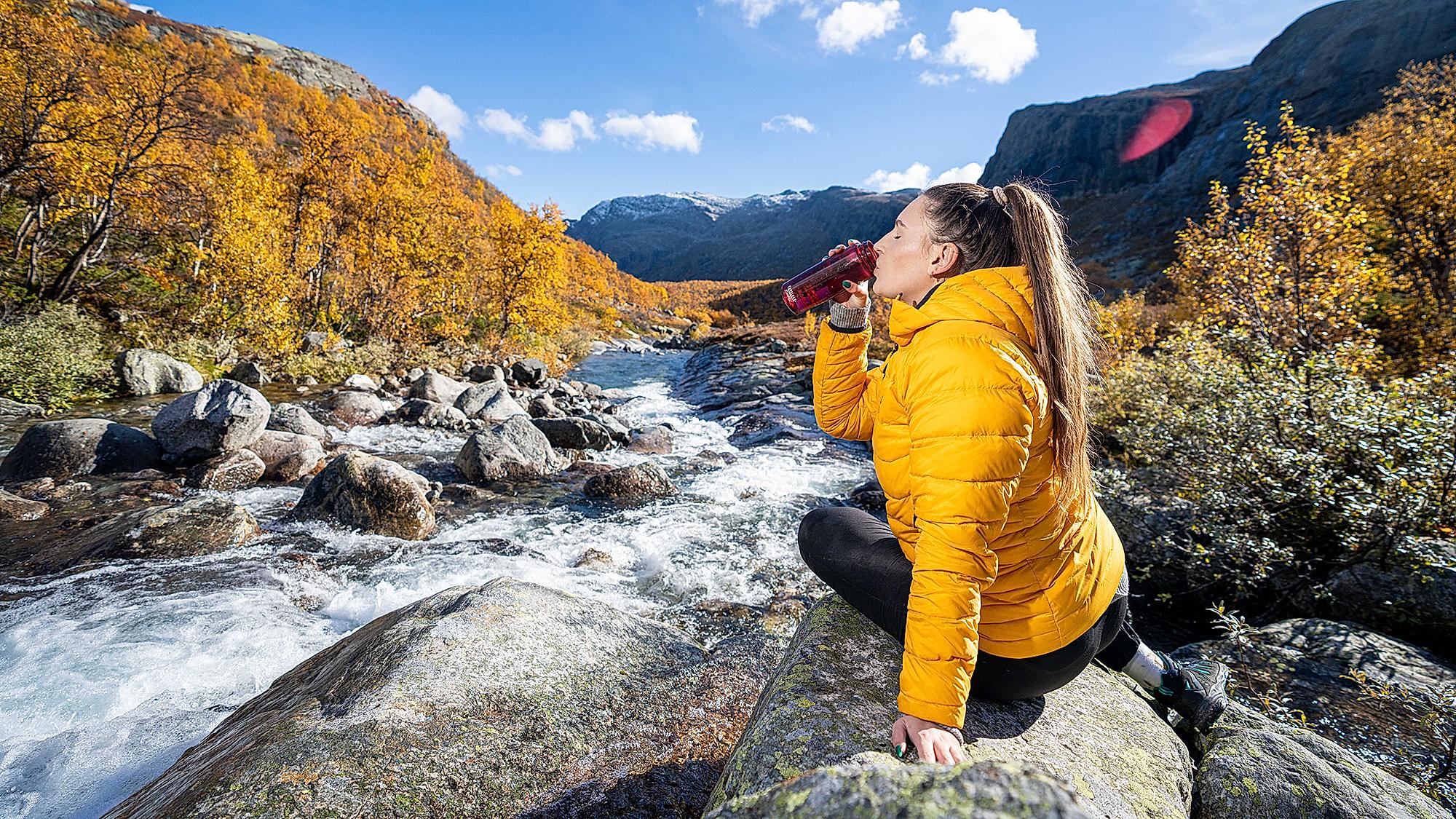 Woman drinking water from a river, Hemsedal, Norway.