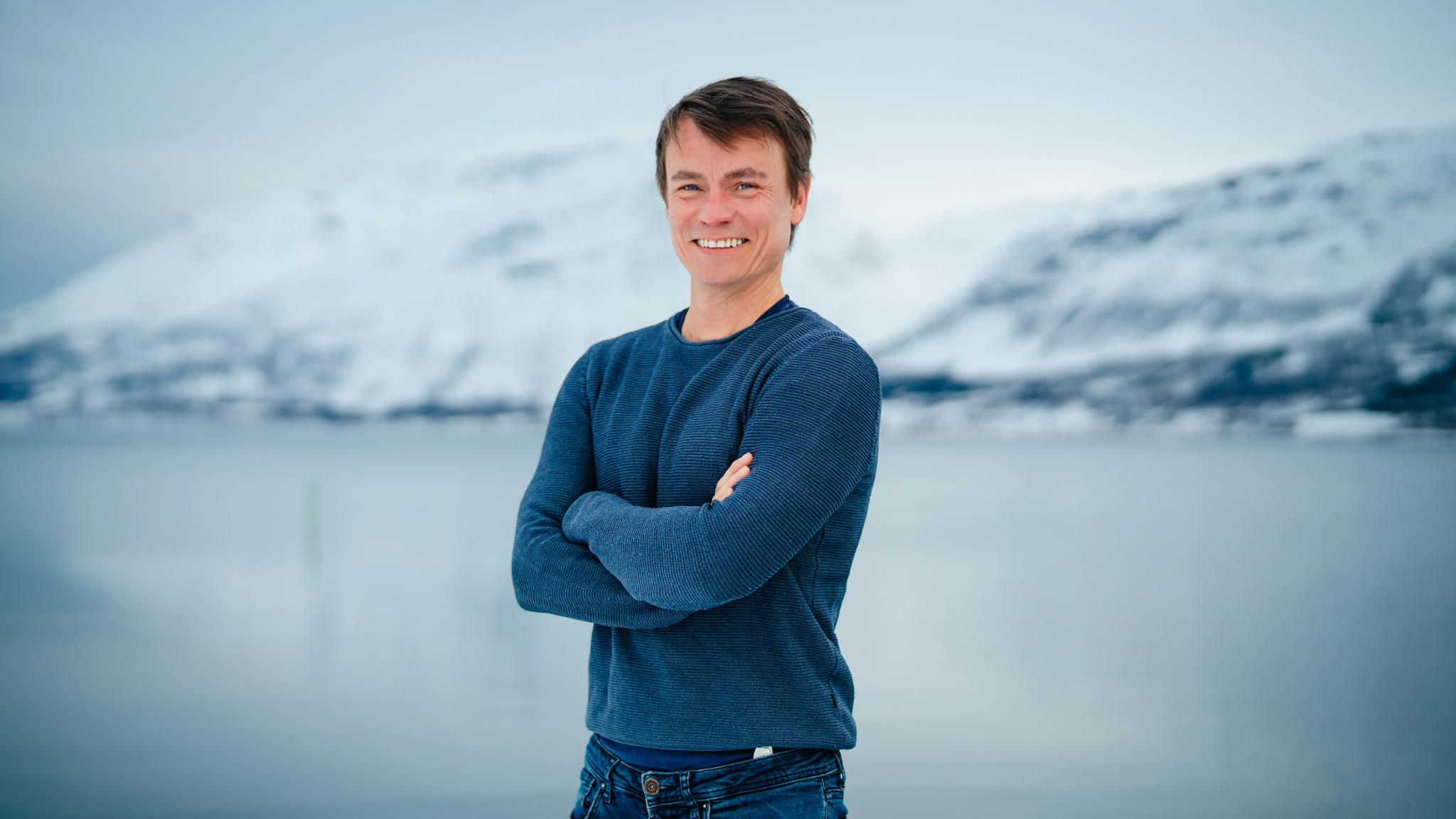 A man standing standing in front of a fjord and a mountain in the winter in Lyngen.