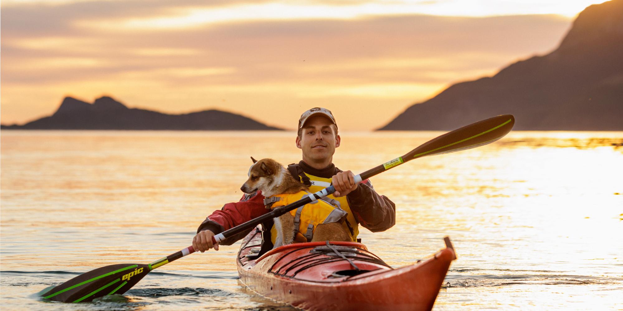 En mann og en hund kjører kajakk i midnattssolen i Nord-Norge.