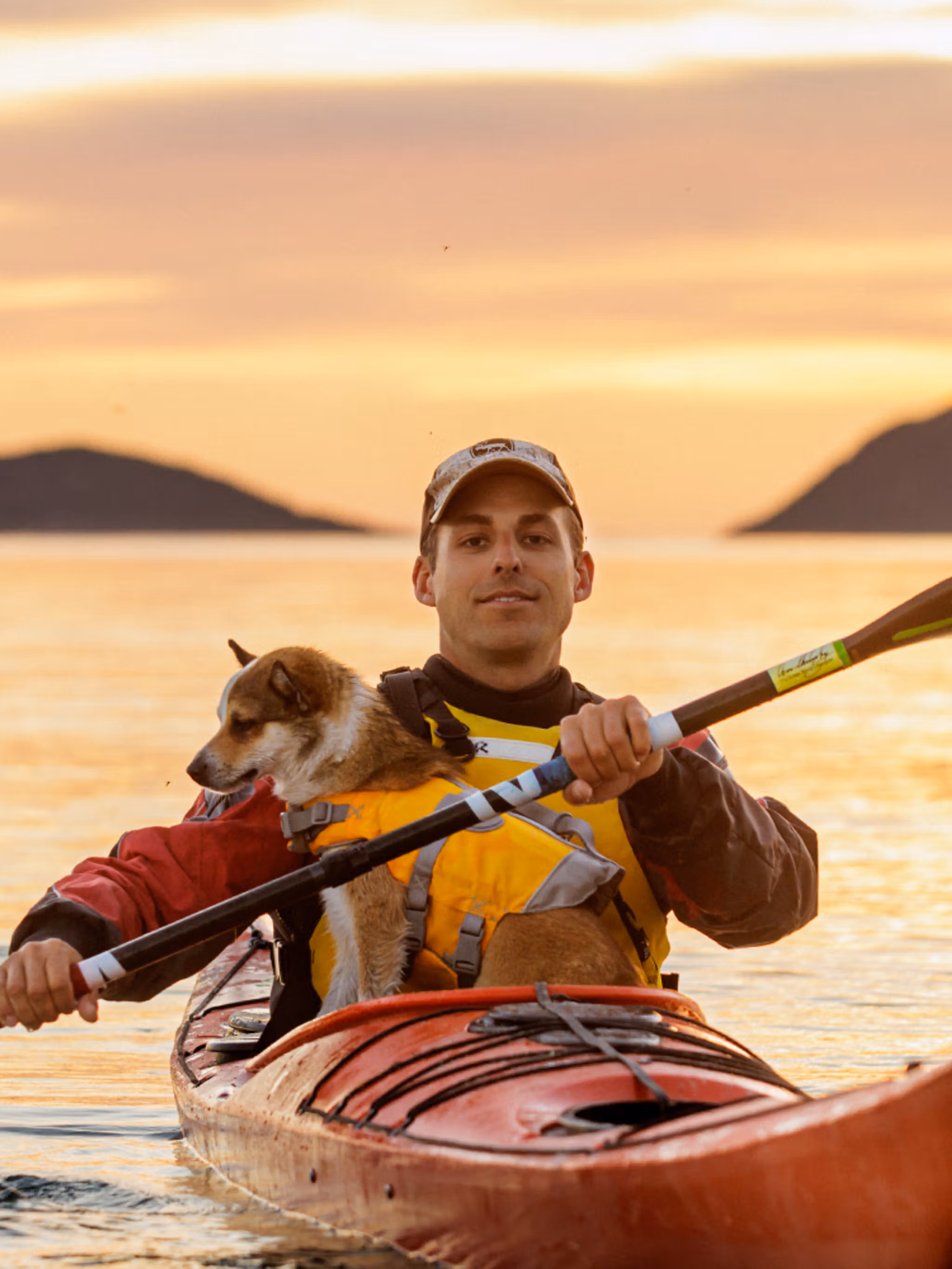 A man and a dog is kayaking in the midnight sun in Northern Norway.