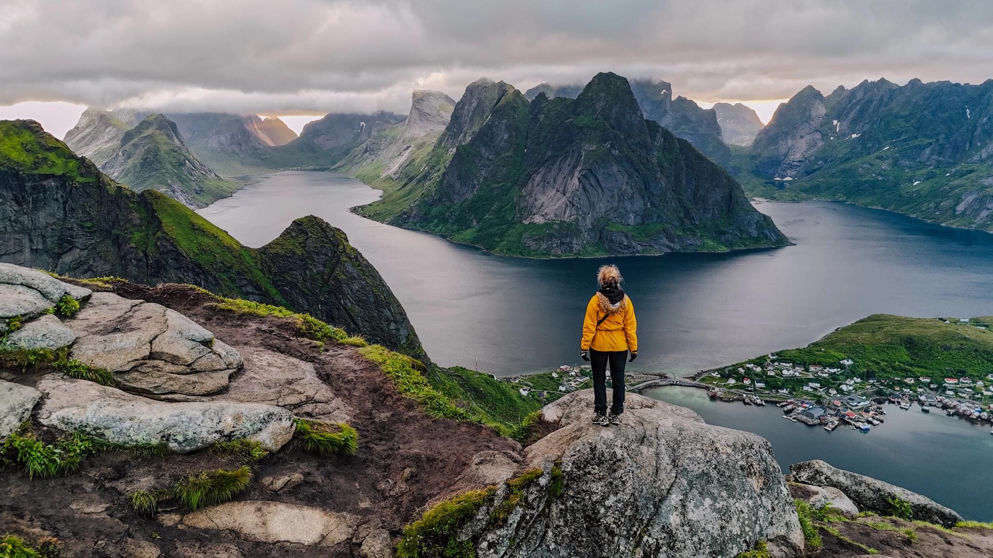 En person står på toppen av Reinebringen i Lofoten.