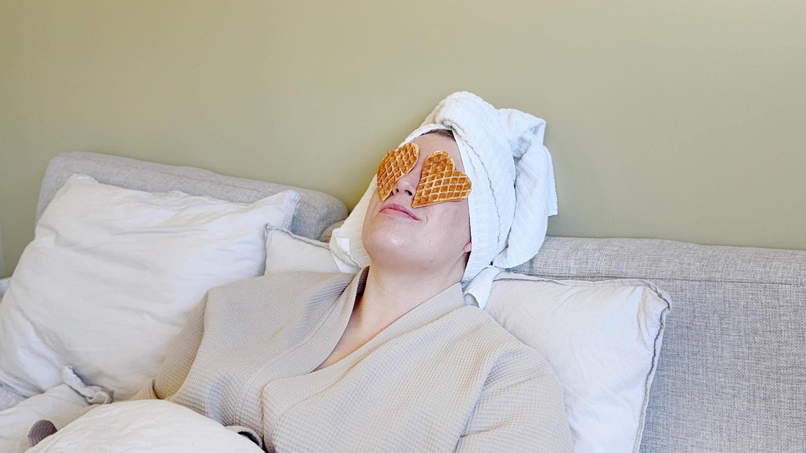 A woman laying in bed with waffles on her eyes.
