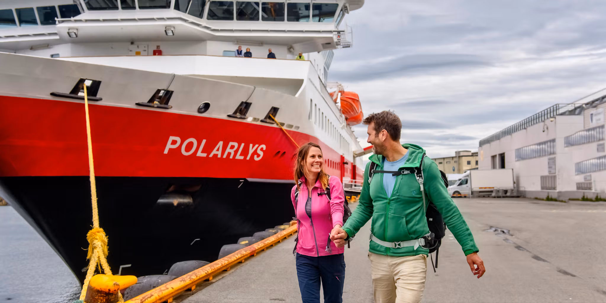 A smiling couple in front of the MS Polarlys Hurtigruten ship in Lofoten, Northern Norway