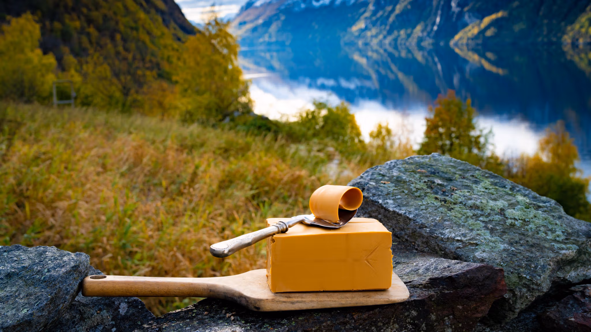 Norwegian brown cheese against a backdrop of mountains and a fjord