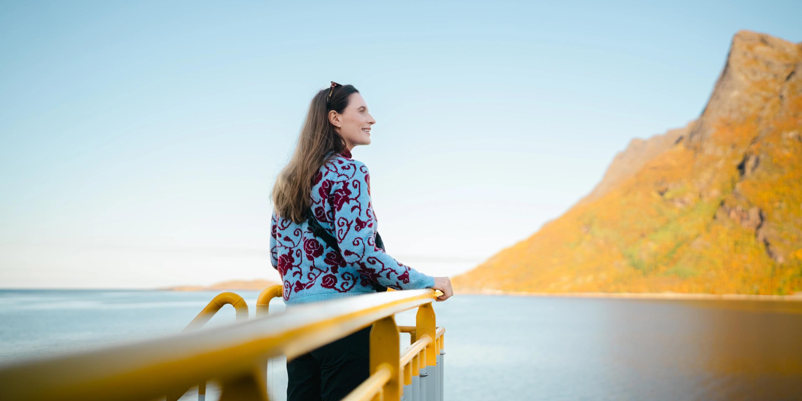 A woman standing on a ferry looking at Kjerringøy, outside og Bodø in Northern Norway.