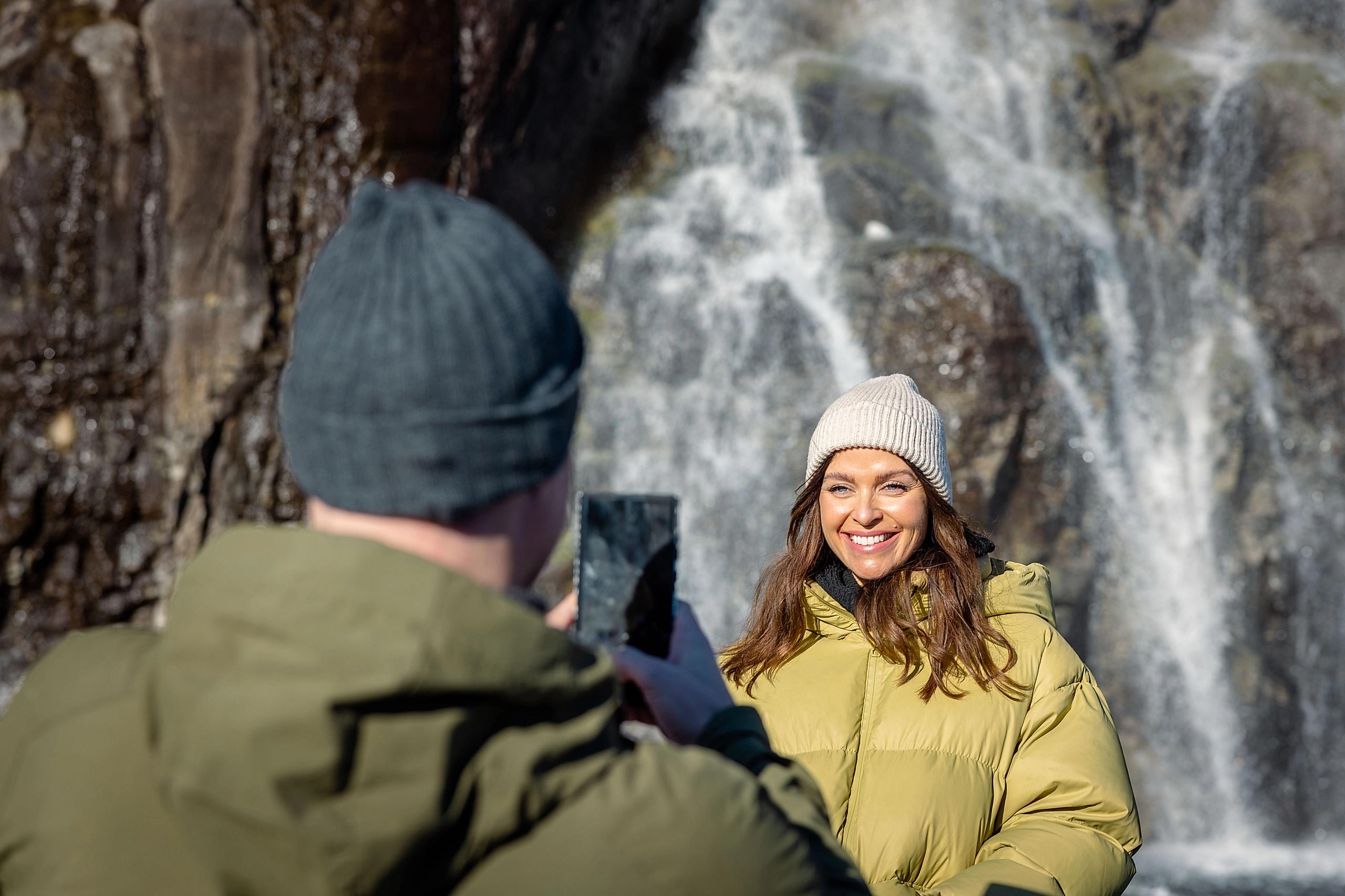 A couple taking pictures of a waterfall.