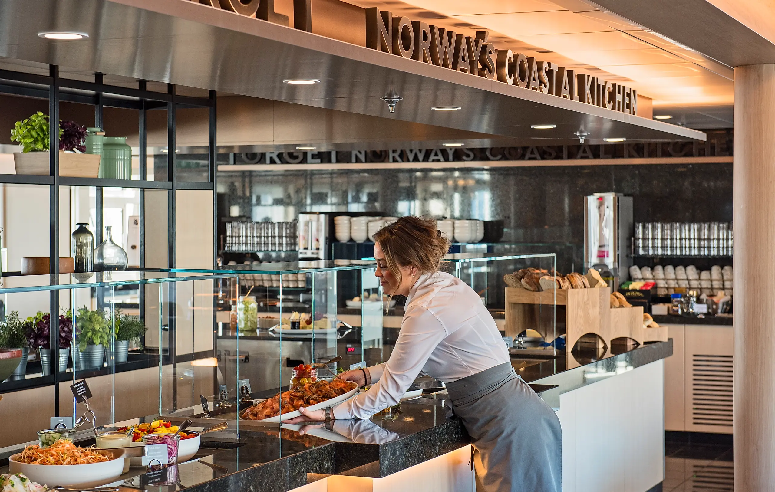 En kvinne som setter frem mat til buffeten på Hurtigruten