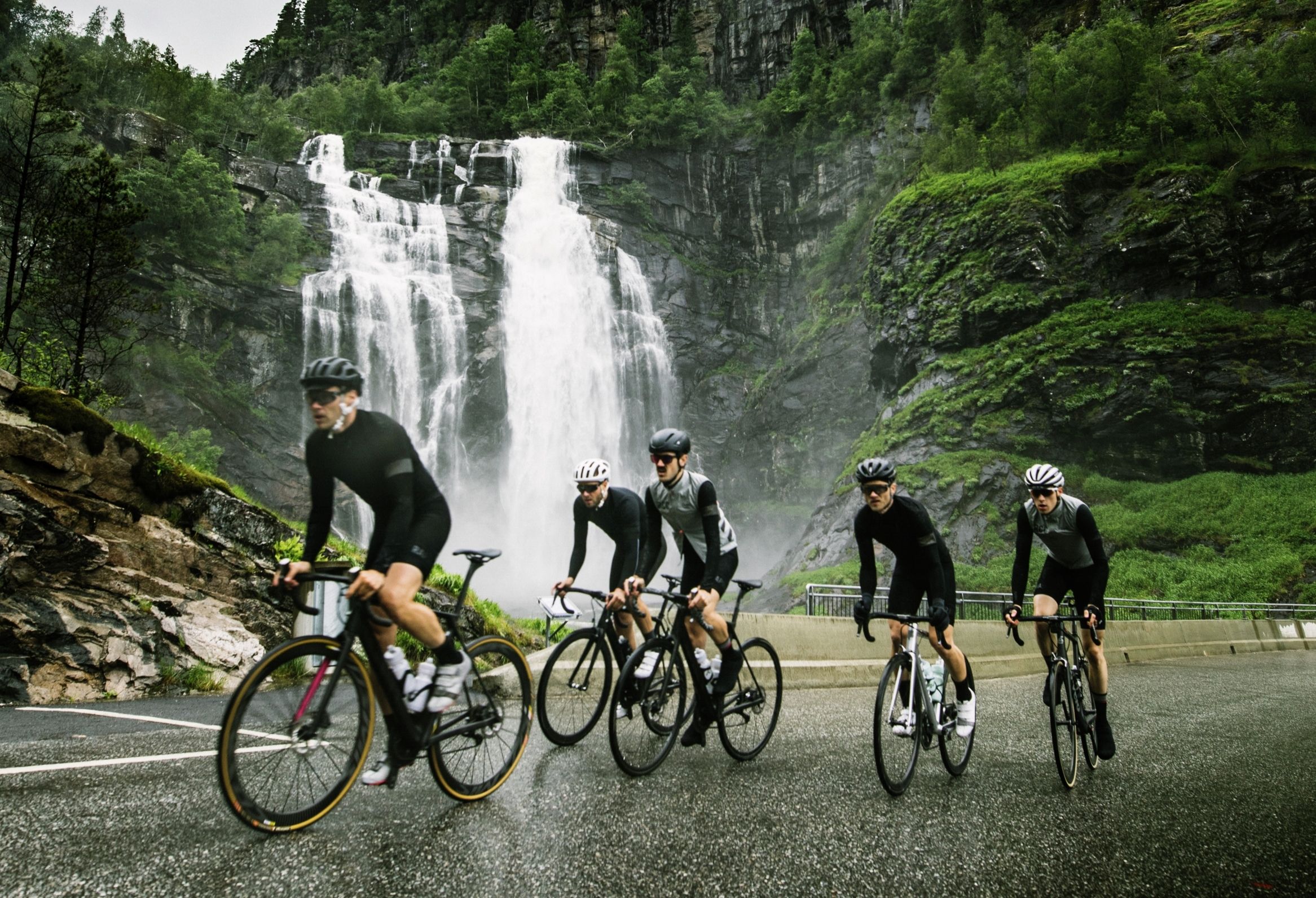 A group of road cyclists in front of a waterfall in Fjord Norway
