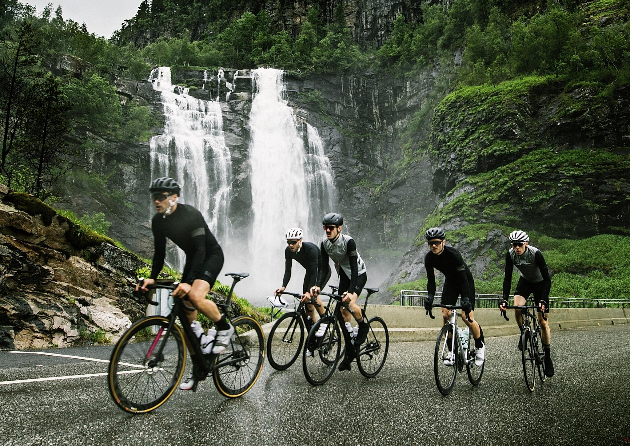 A group of road cyclists in front of a waterfall in Fjord Norway