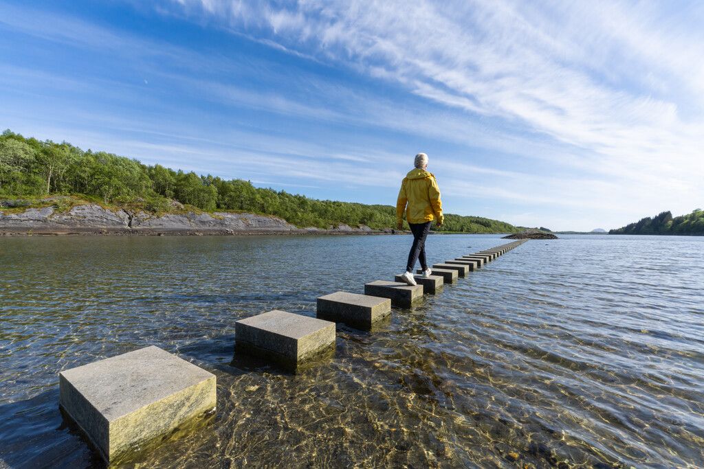 A woman walking on stepping stones in the sea.