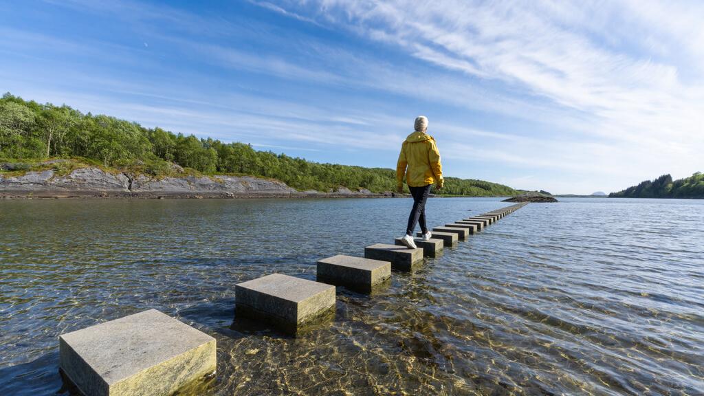 A woman walking on stepping stones in the sea.