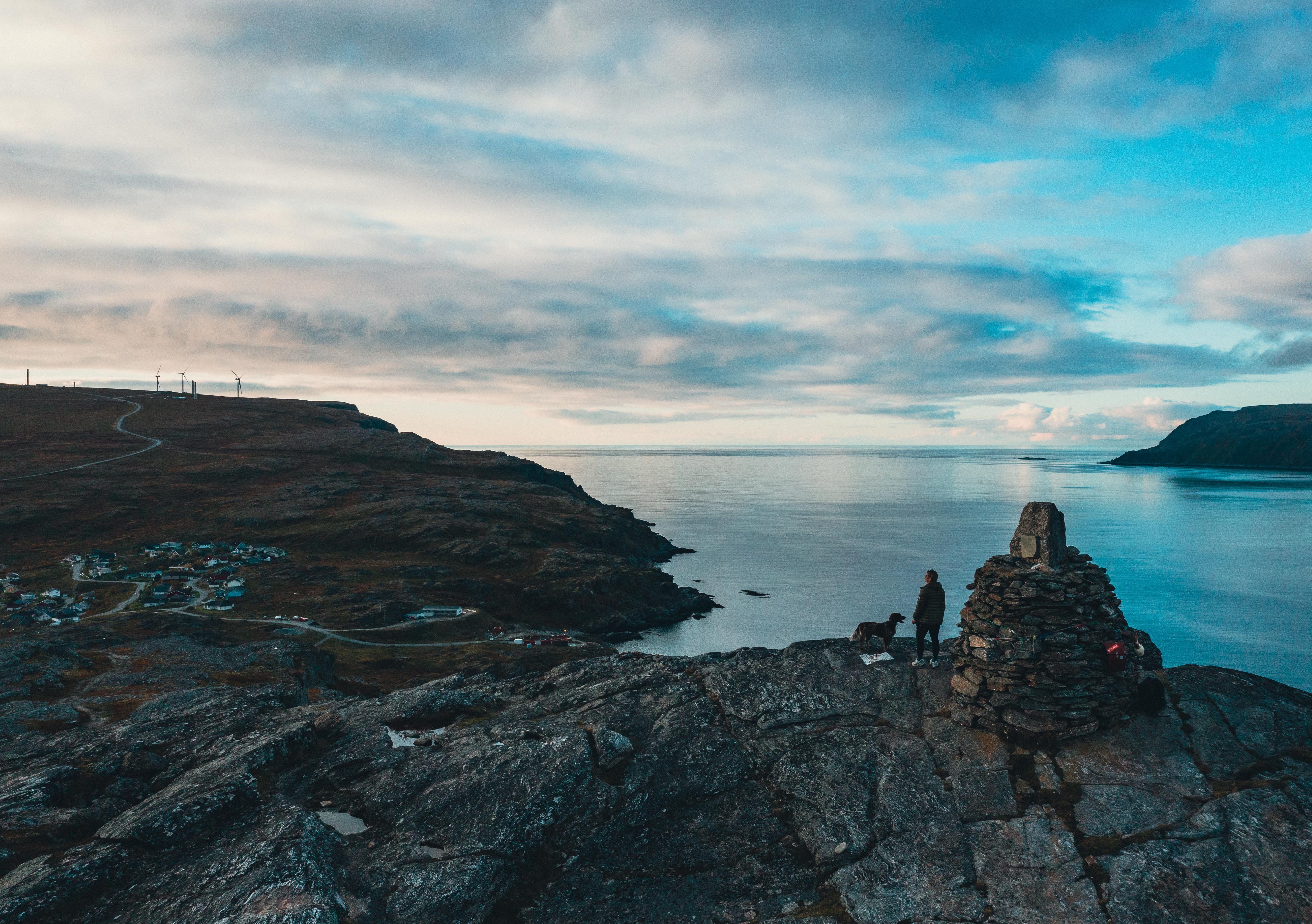 A person and a dog standing on a mountain overlooking Havøysund village