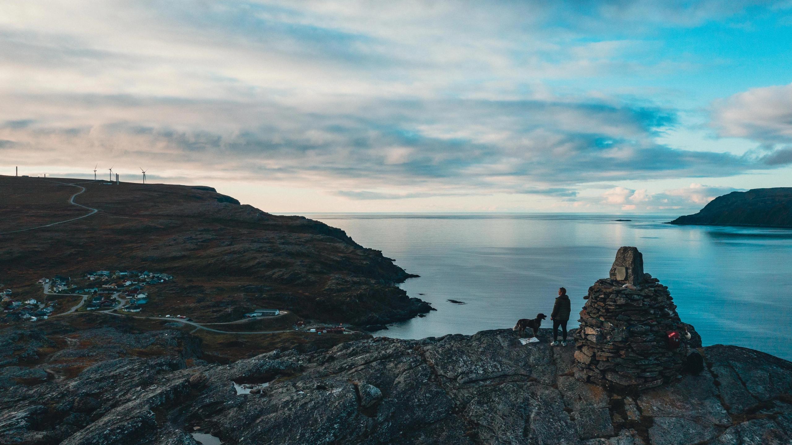 A person and a dog standing on a mountain overlooking Havøysund village