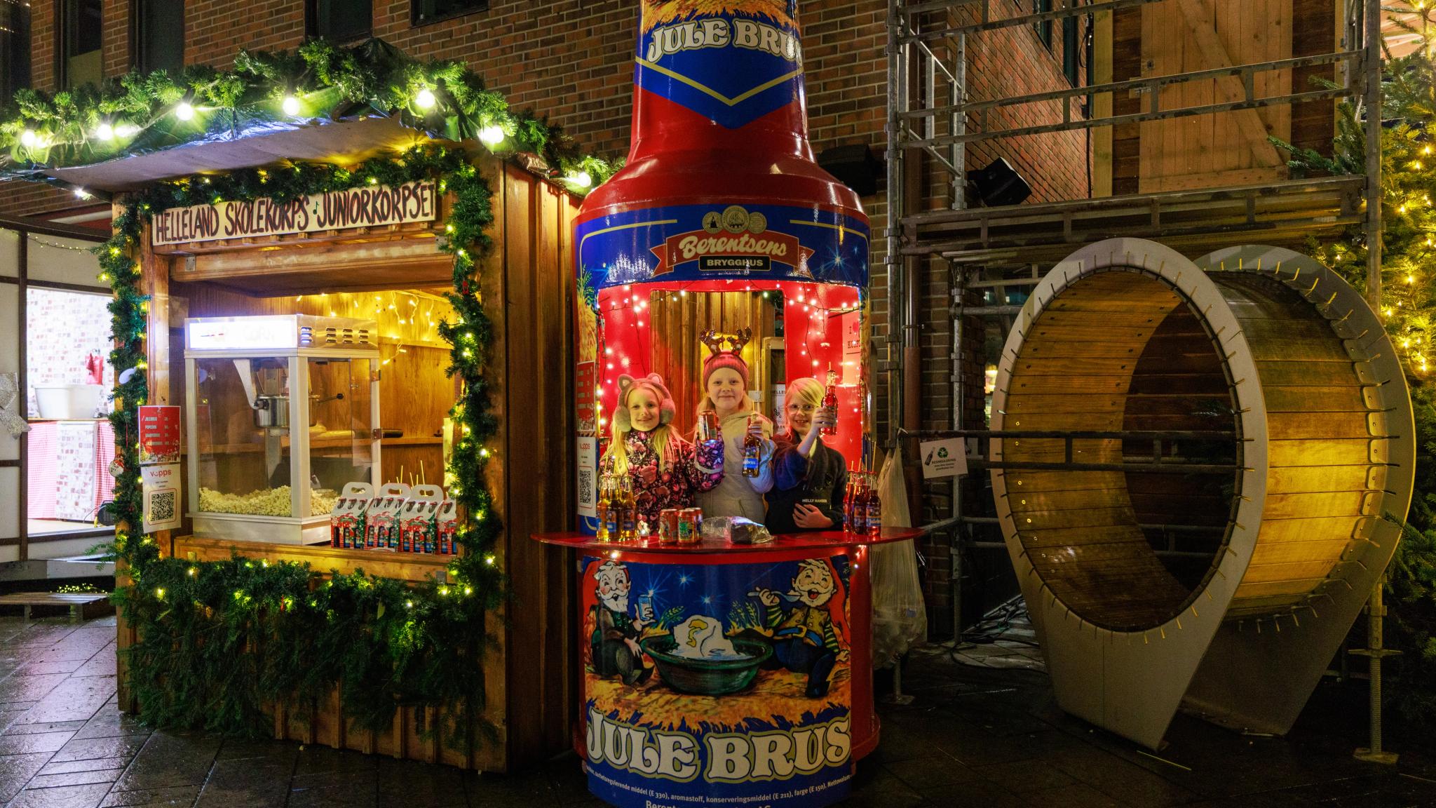 Three young girls inside a Christmas soda shaped stall at Egersund Christmas market