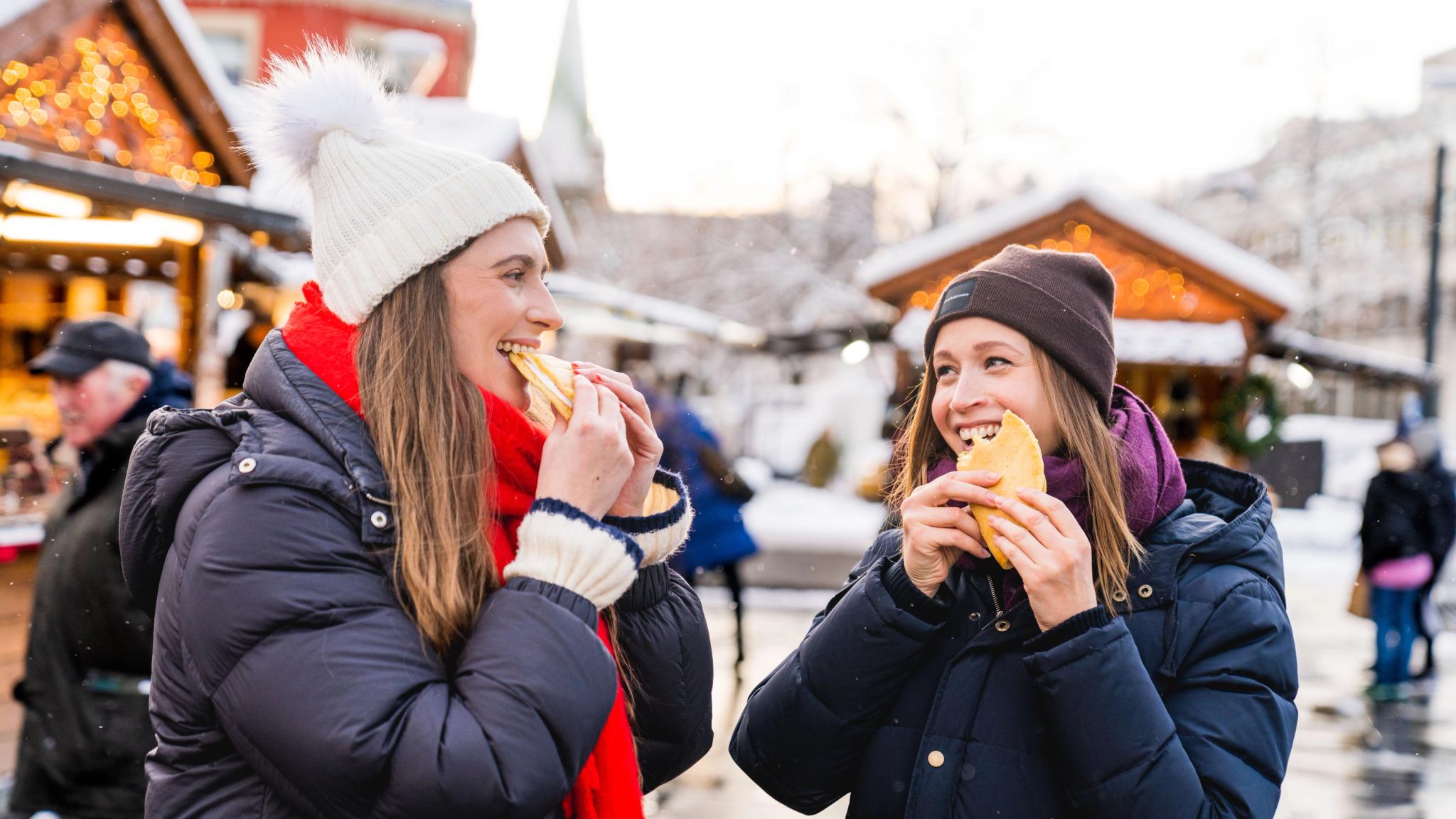 Two persons eating sveler at the Christmas market in Trondheim, Trøndelag, Norge.