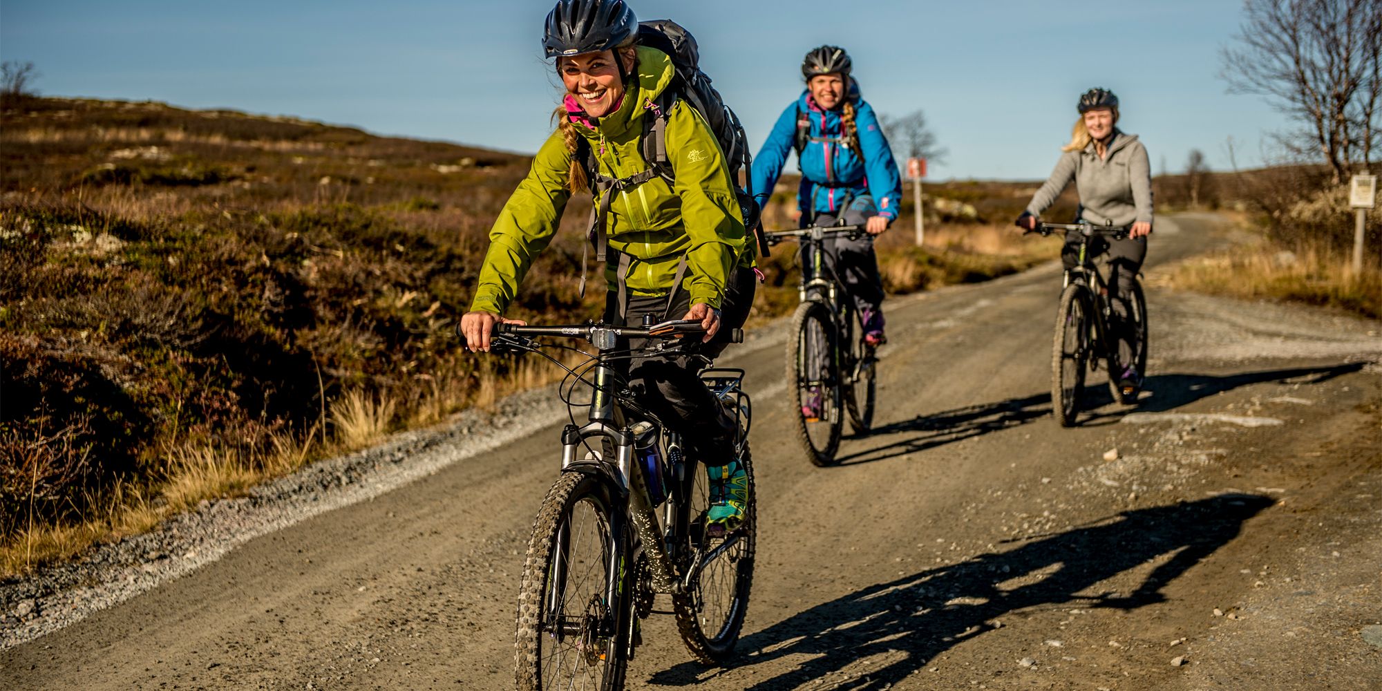 Three people cycling at a dirt road on the Hardangervidda mountain plateau in Eastern Norway