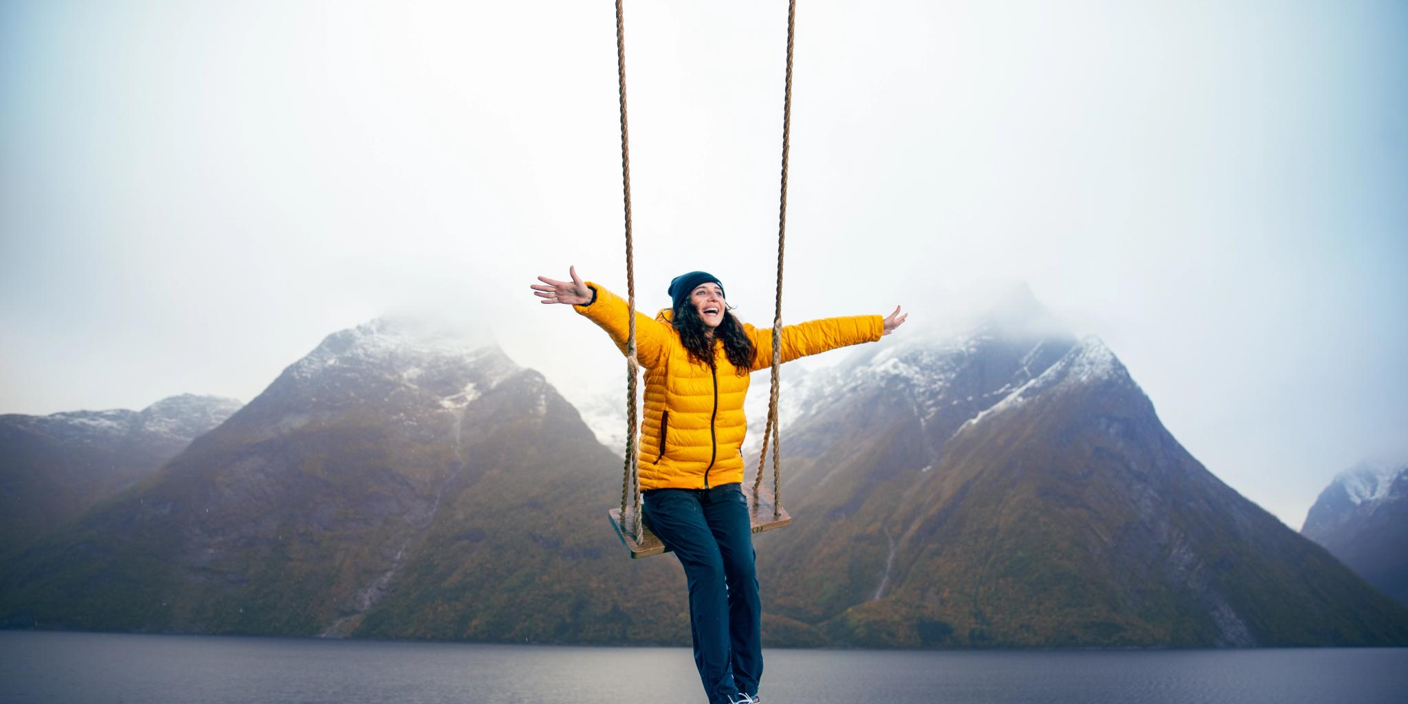 A person on a swing with a view of snow-clad mountains and the Hjørundfjord in Fjord Norway