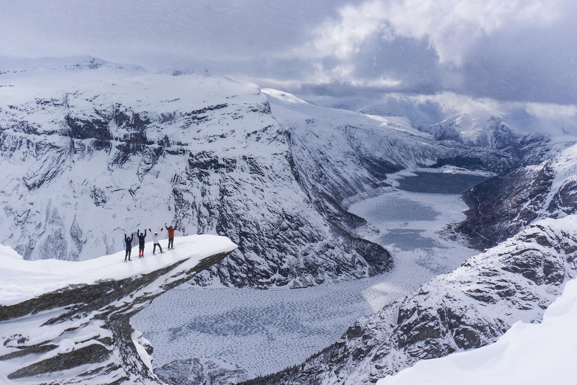 Vier Personen mit Schneeschuhen stehen oben auf der Trolltunga in Fjord Norwegen im Winter