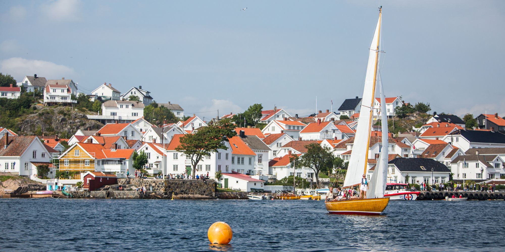 A wooden sailboat sailing in front of white-painted wooden houses in Risør, Southern Norway