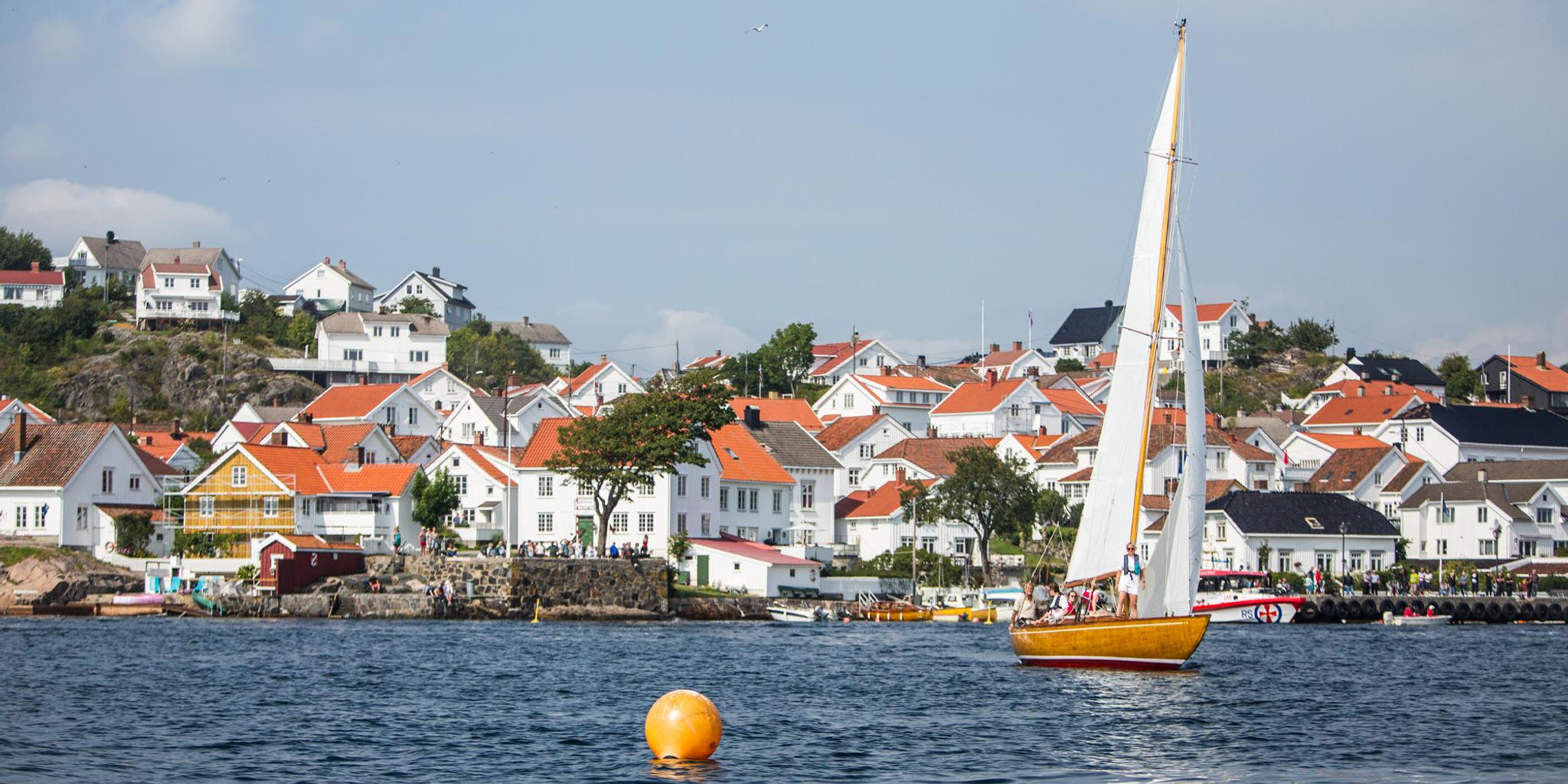A wooden sailboat sailing in front of white-painted wooden houses in Risør, Southern Norway