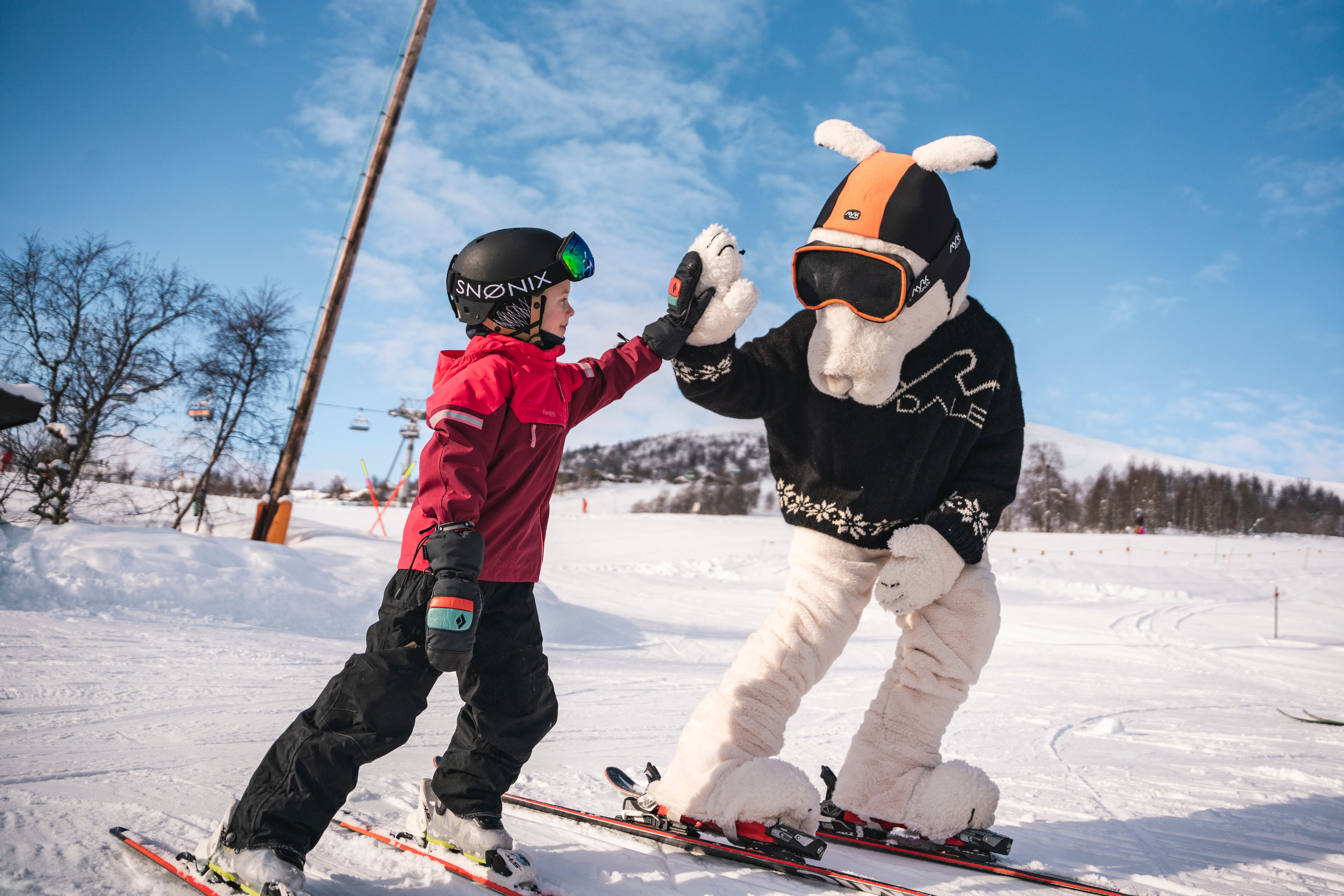 A child and a mascot on alpine skiis, giving each other a high five.
