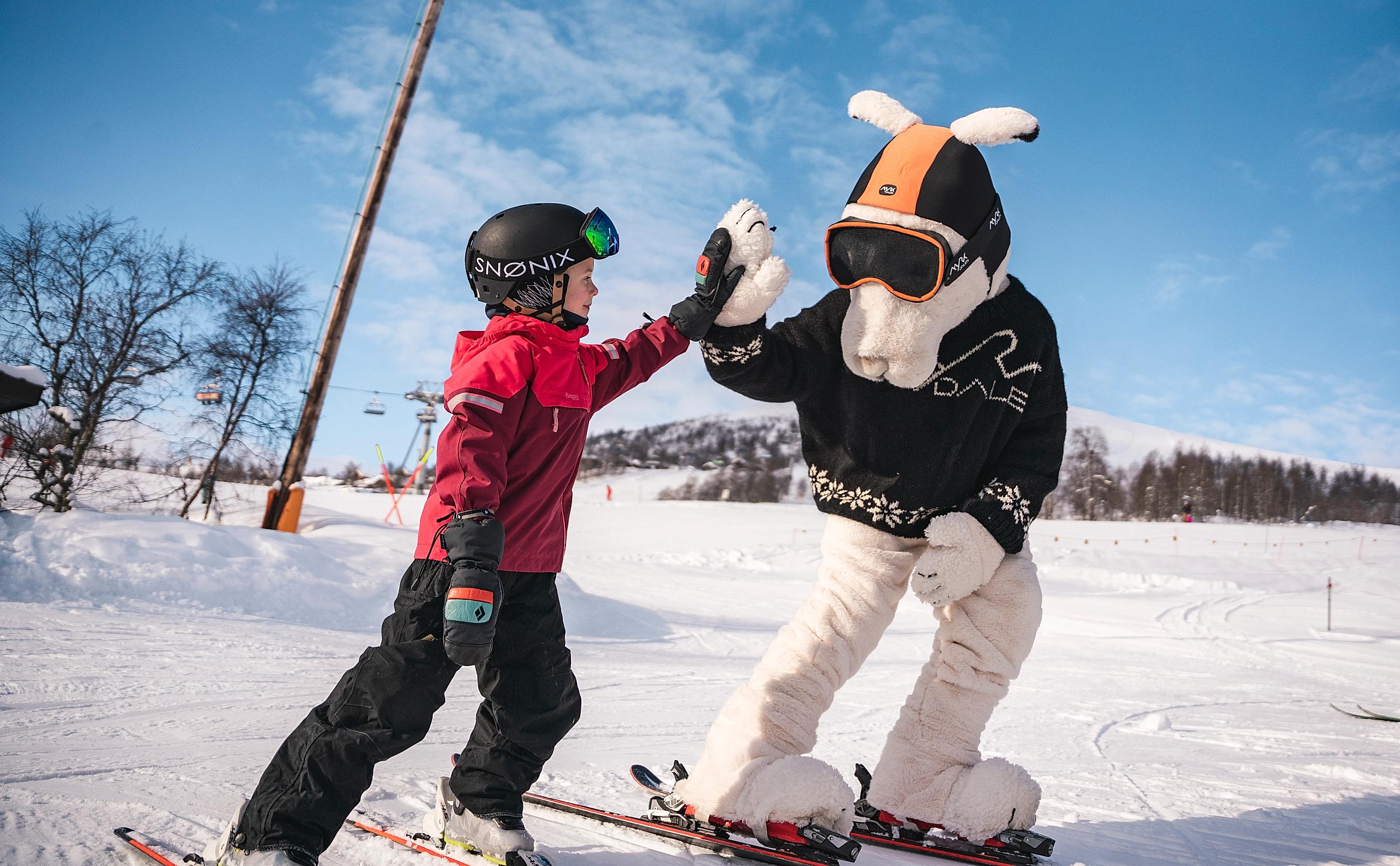 A child and a mascot on alpine skiis, giving each other a high five.