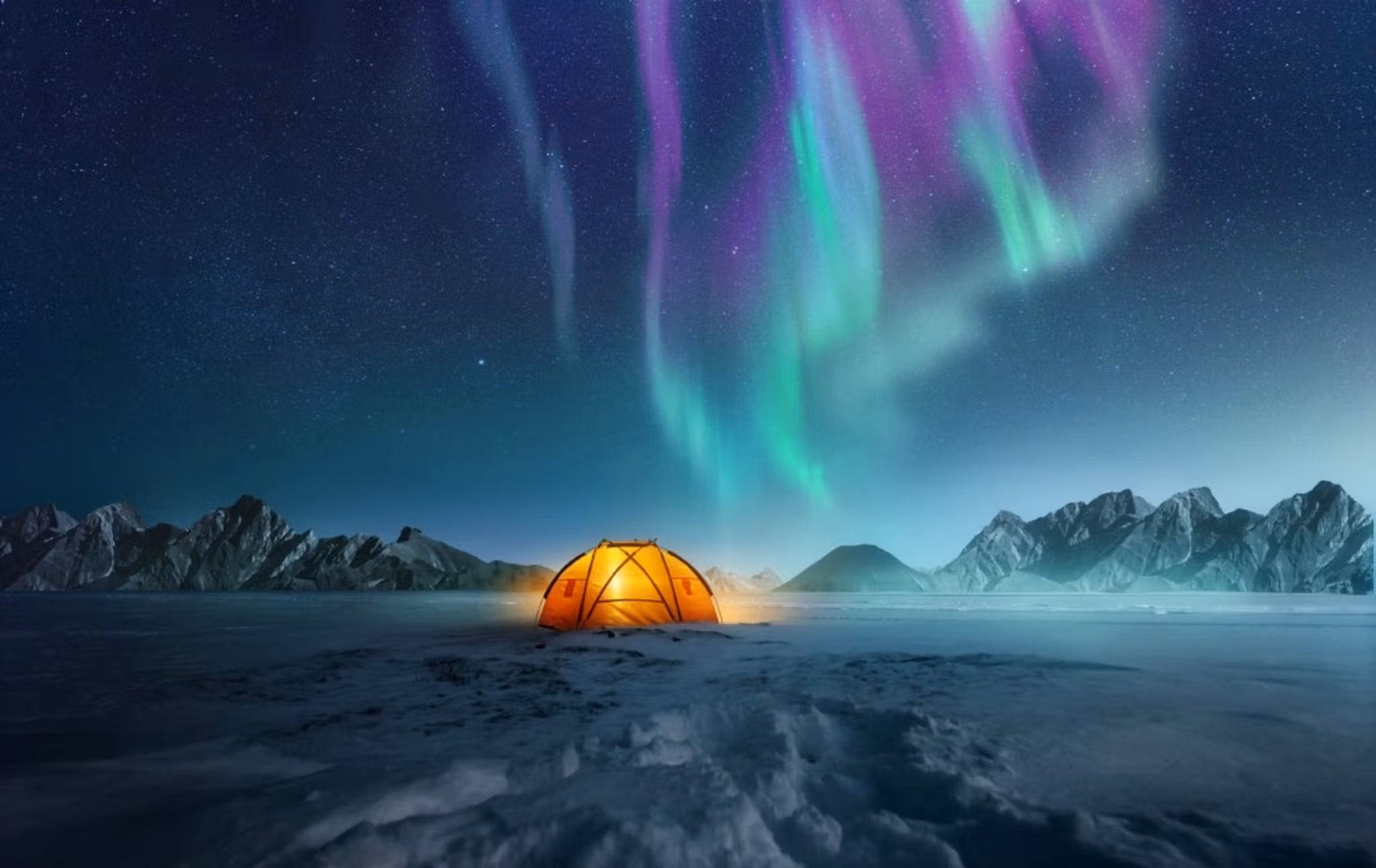 Lit-up tent in snow with colorful northern lights and mountains behind it