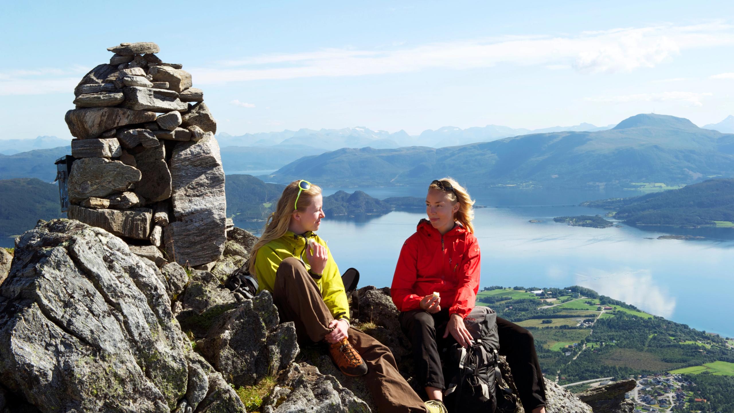 To dammer sitter ved en varde på toppen av Freikollen i Kristiansund på Vestlandet. Fjell og fjord i bakgrunnen.