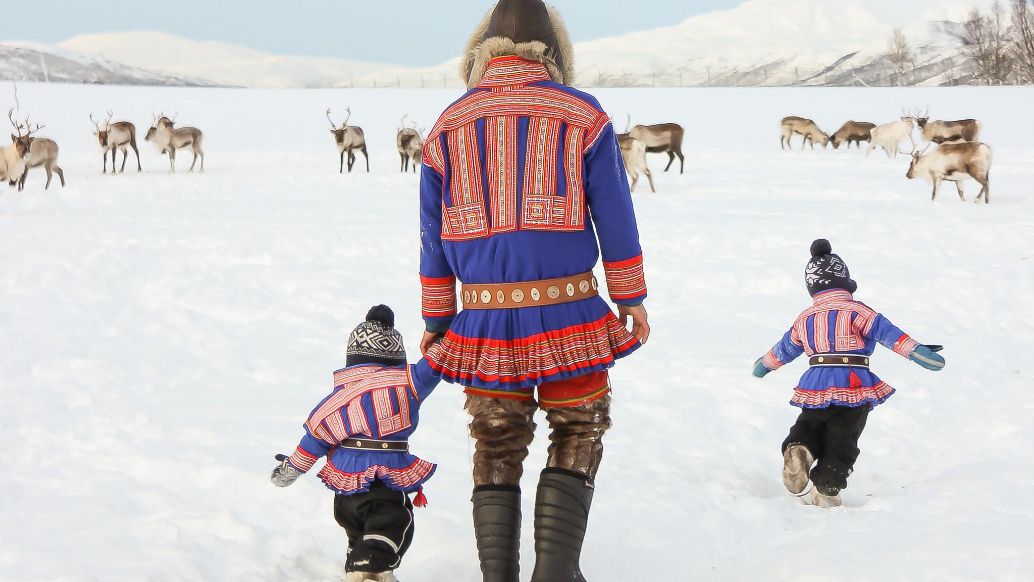 Sami children and their father wearing kofter in the snow