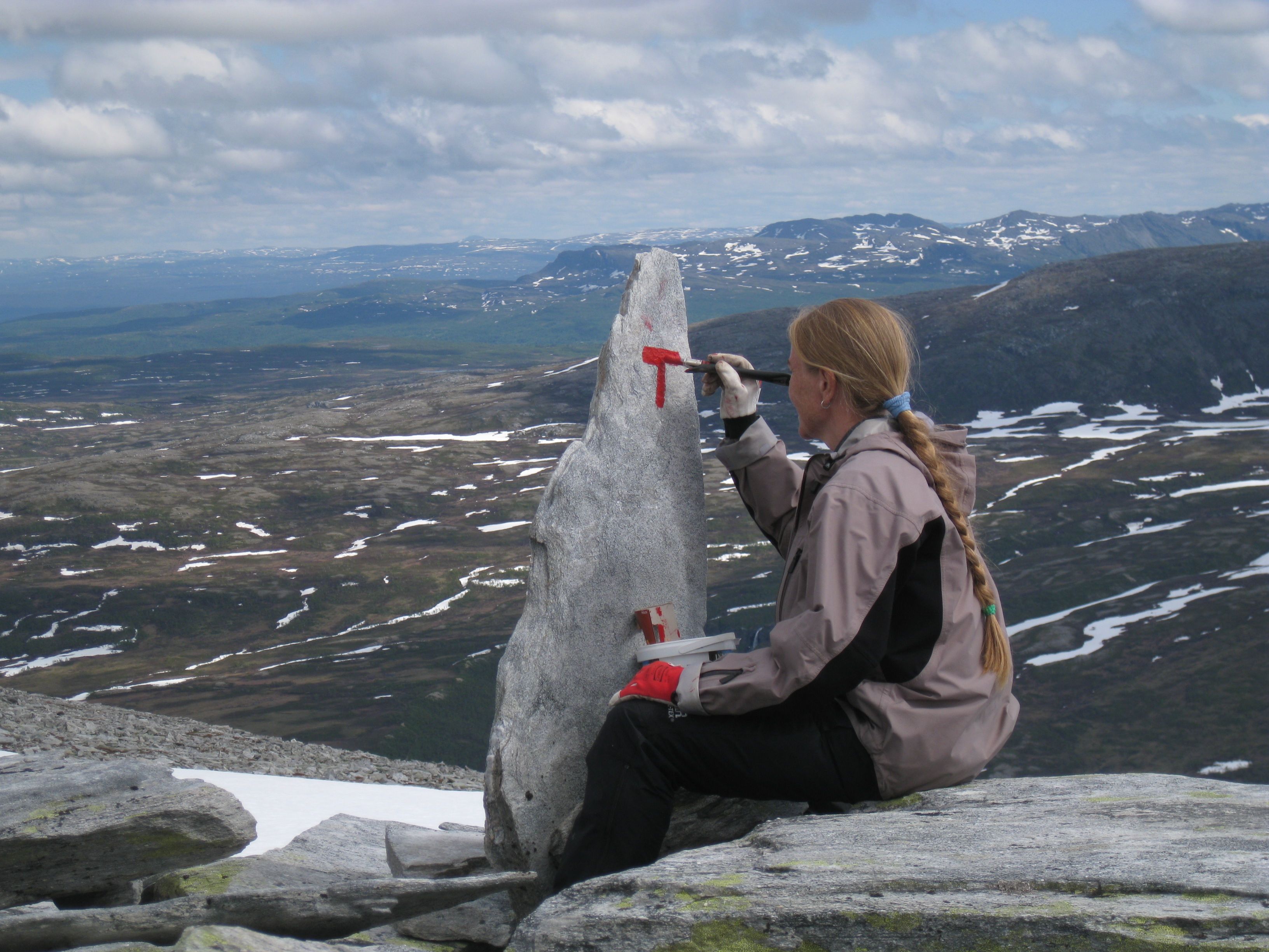 Jorid Rajala of DNT, painting signs along a hiking trail with a nice mountain view in the background